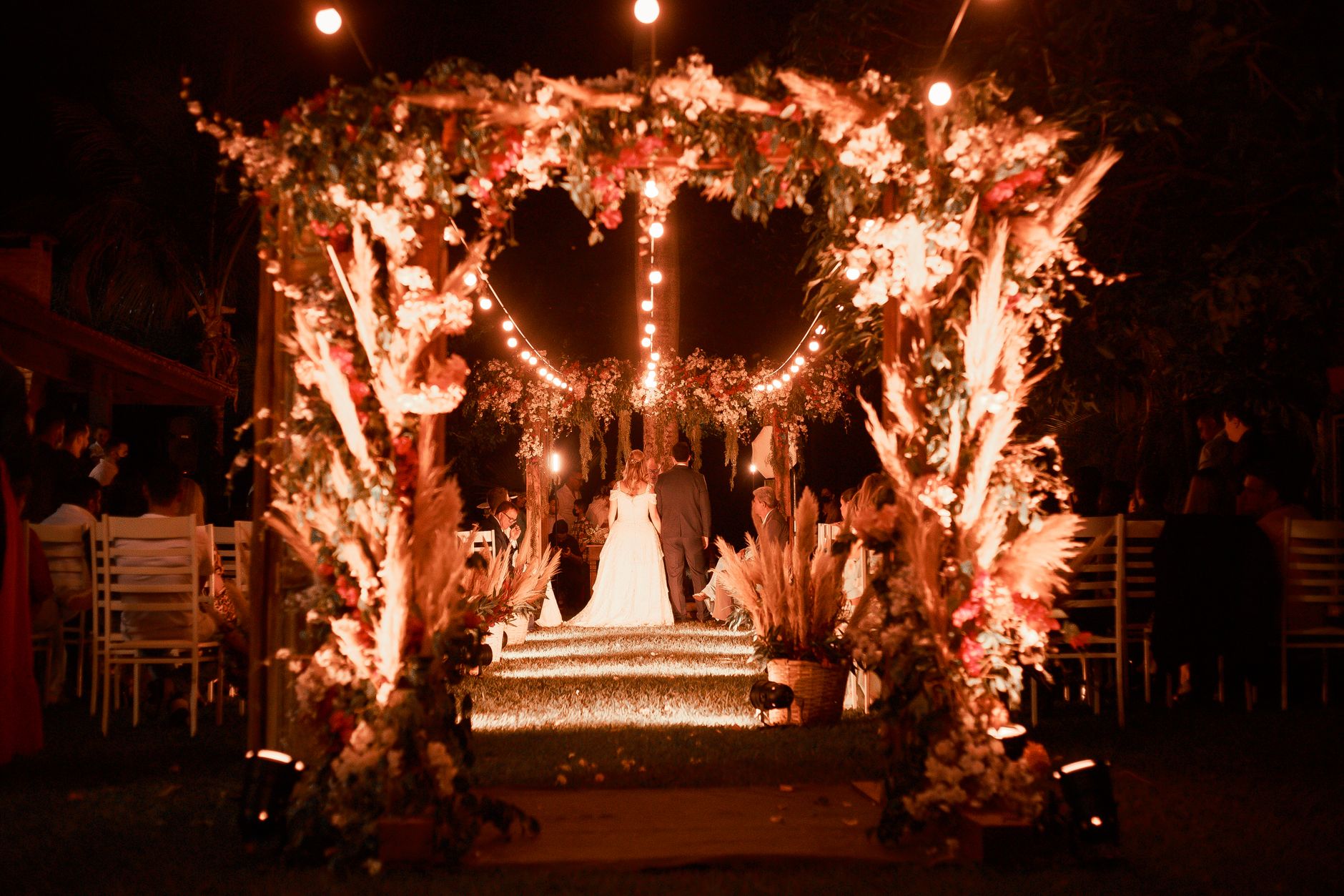 Enchanting wedding ceremony under an illuminated floral arch at night